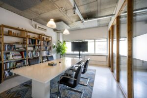 Vergaderruimte aan de Anthony Fokkerweg met een grote tafel, boekenrekken, een flatscreen en industriële plafondafwerking.